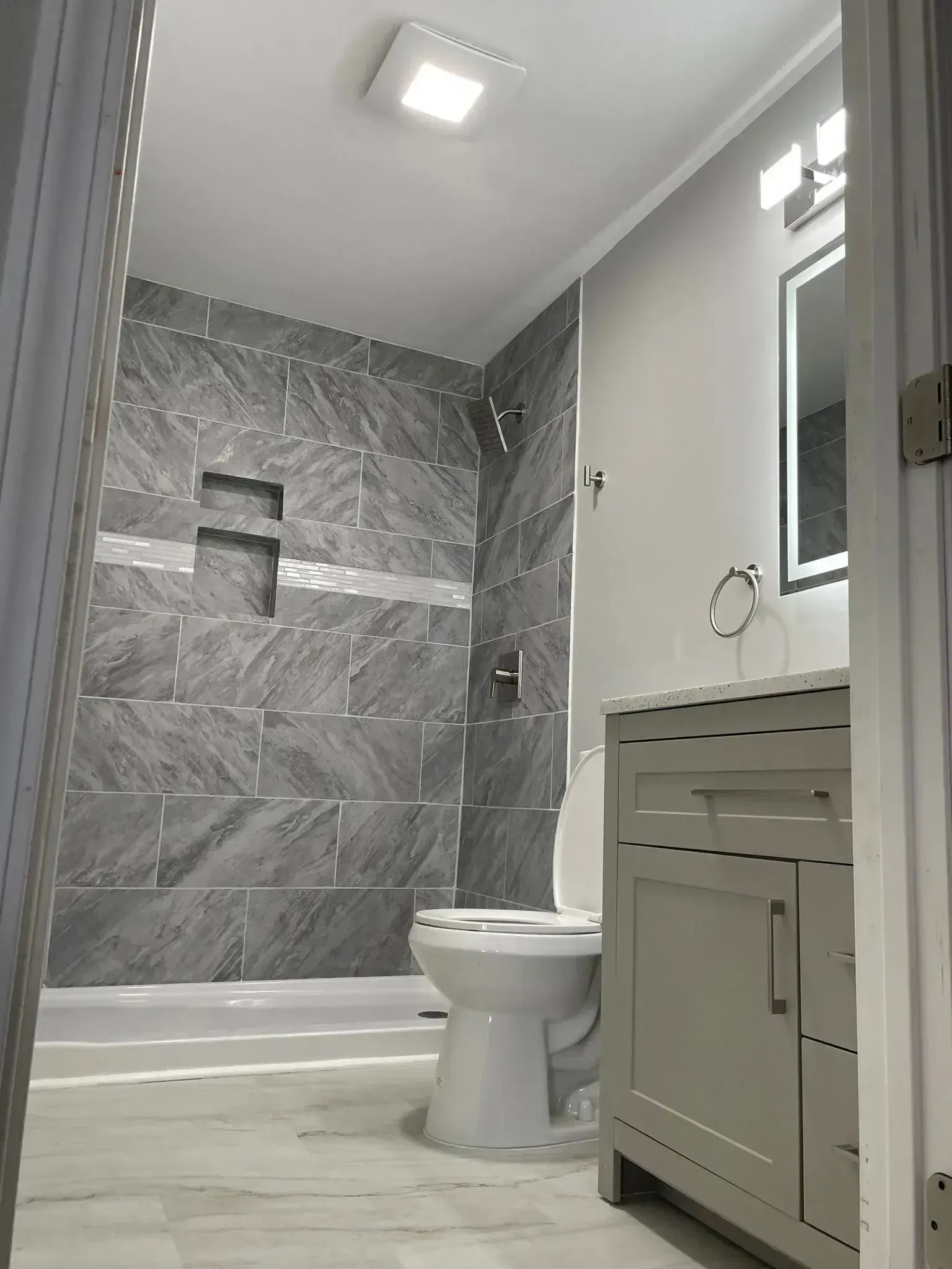 Modern bathroom with gray marble tile, a toilet, and a vanity under bright ceiling lights