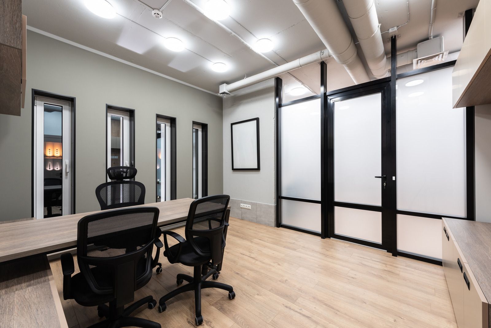 Modern office with desks, rolling chairs, frosted glass walls, and light wood flooring