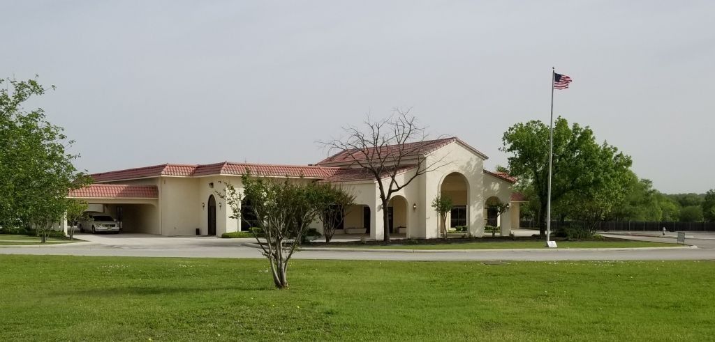 Cream-colored building with red tile roof, American flag, and green lawn.