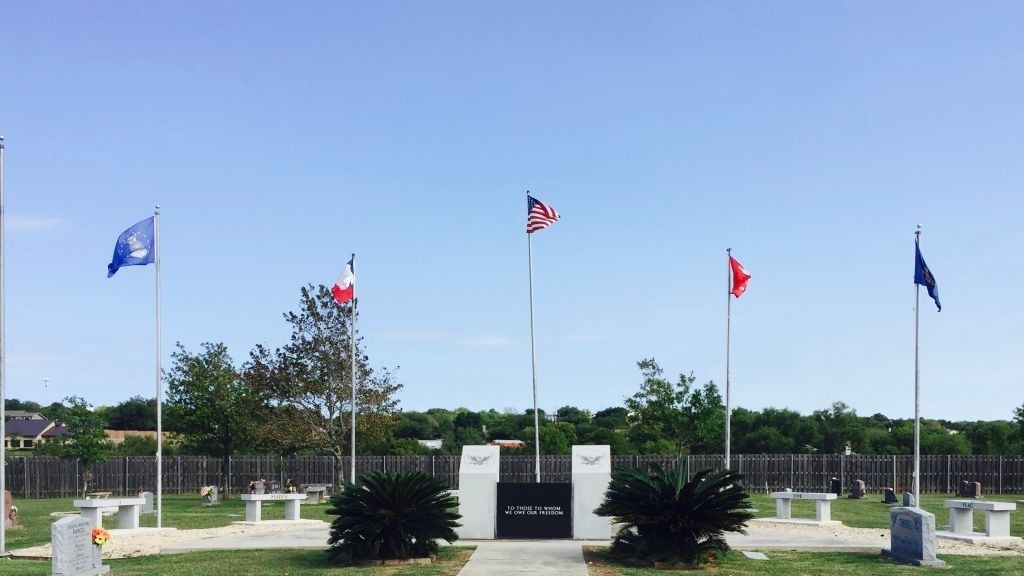 Flags of various colors fly in a memorial setting.