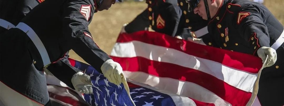 Marines fold an American flag, red and white stripes and blue field with white stars visible.