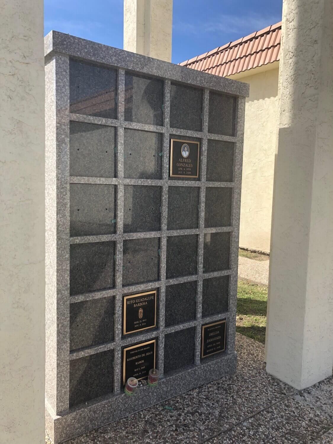 A granite columbarium with bronze plaques set in a sunny outdoor setting.