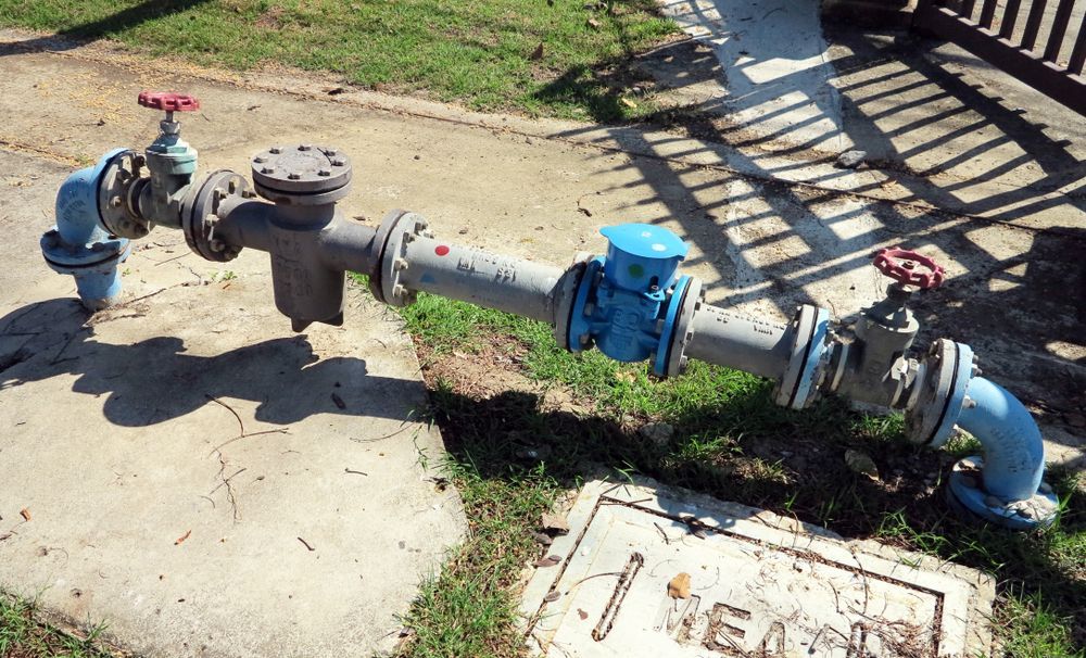 Blue and Gray Water Pipes With Red and Blue Valves on Concrete and Grass — Harwood Plumbing & Gasfitting Pty Ltd in Alawa, NT