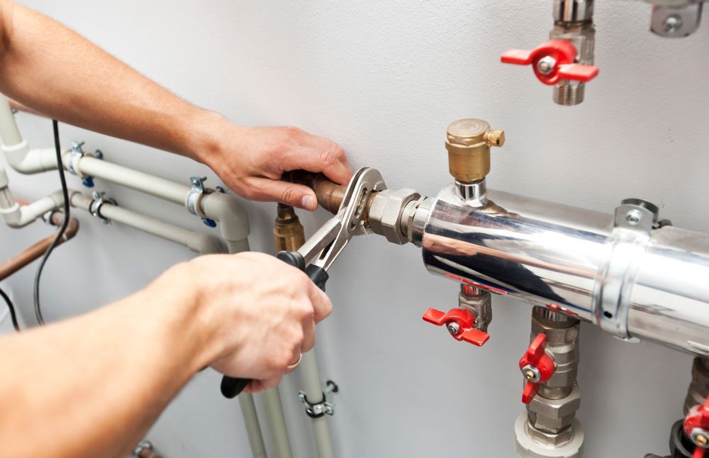 Plumber Using a Wrench to Tighten a Metal Fitting on Pipes Against a White Wall — Harwood Plumbing & Gasfitting Pty Ltd in Alawa, NT