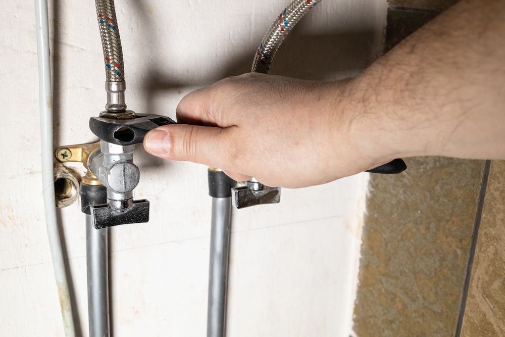 Hand Turning a Black Valve on A Water Pipe in A Utility Room — Harwood Plumbing & Gasfitting Pty Ltd in Alawa, NT