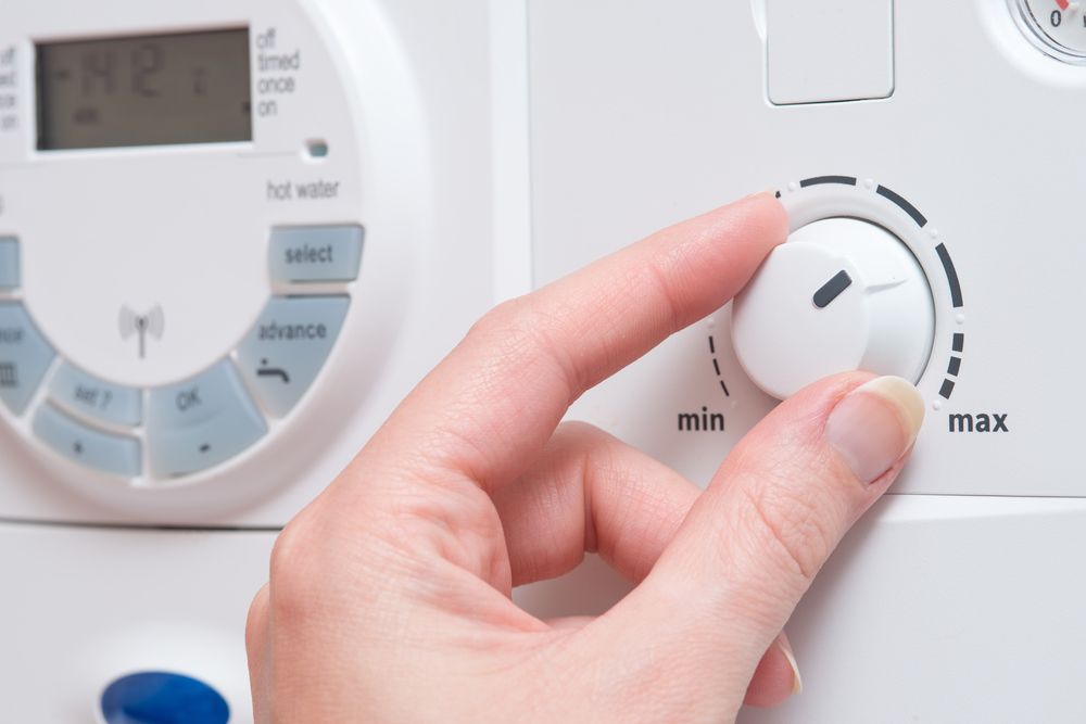 Hand Turning a White Dial on A Boiler Control Panel from