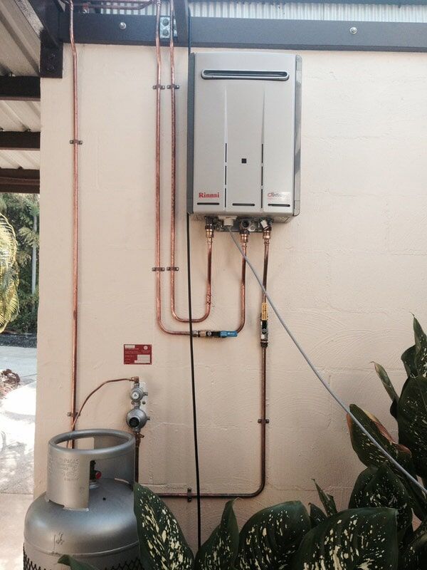 Gas Water Heater Installed Outside on a Beige Wall With Copper Pipes — Harwood Plumbing & Gasfitting Pty Ltd in Alawa, NT