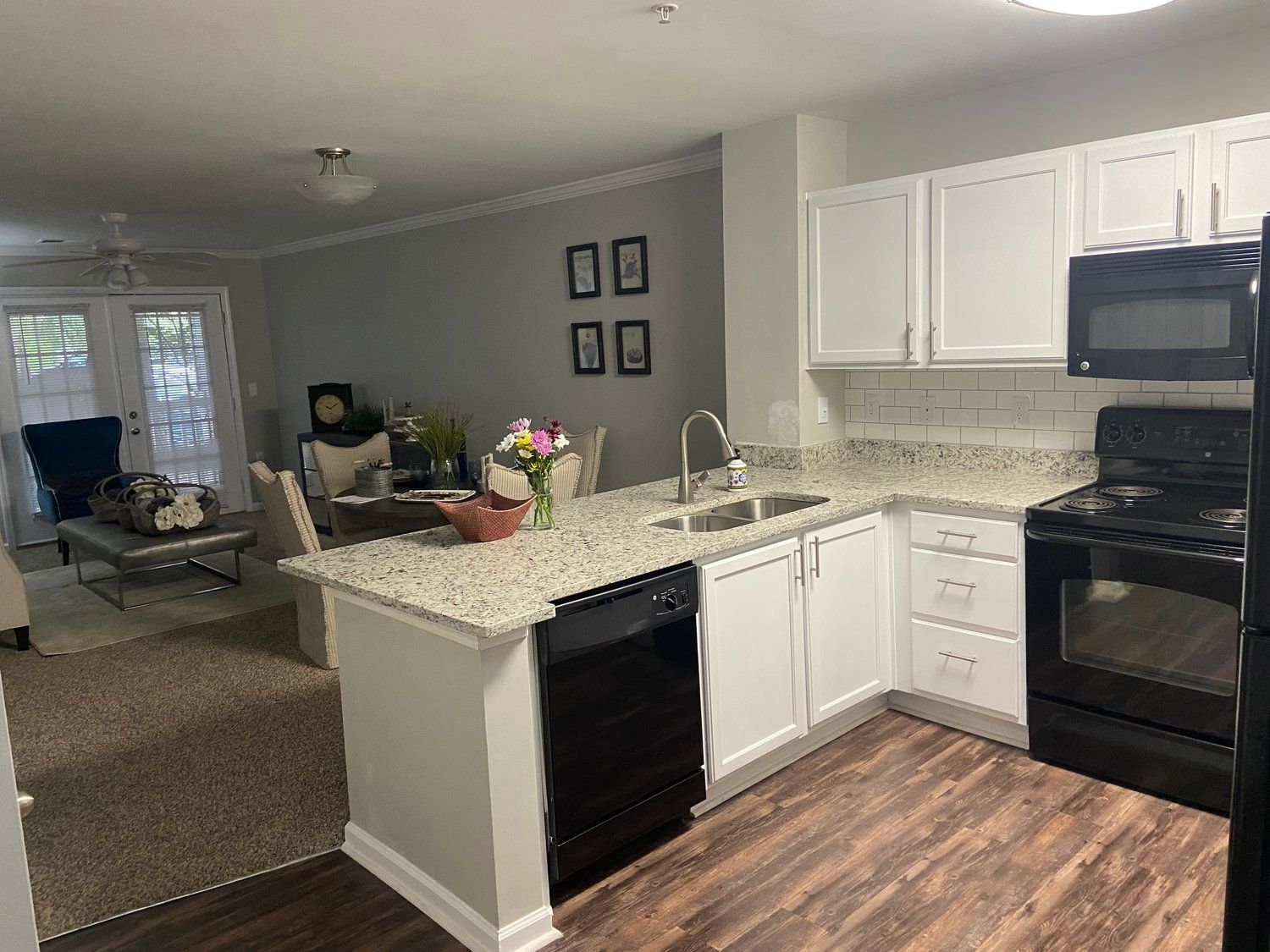 A kitchen with white cabinets , black appliances , granite counter tops and a stove.