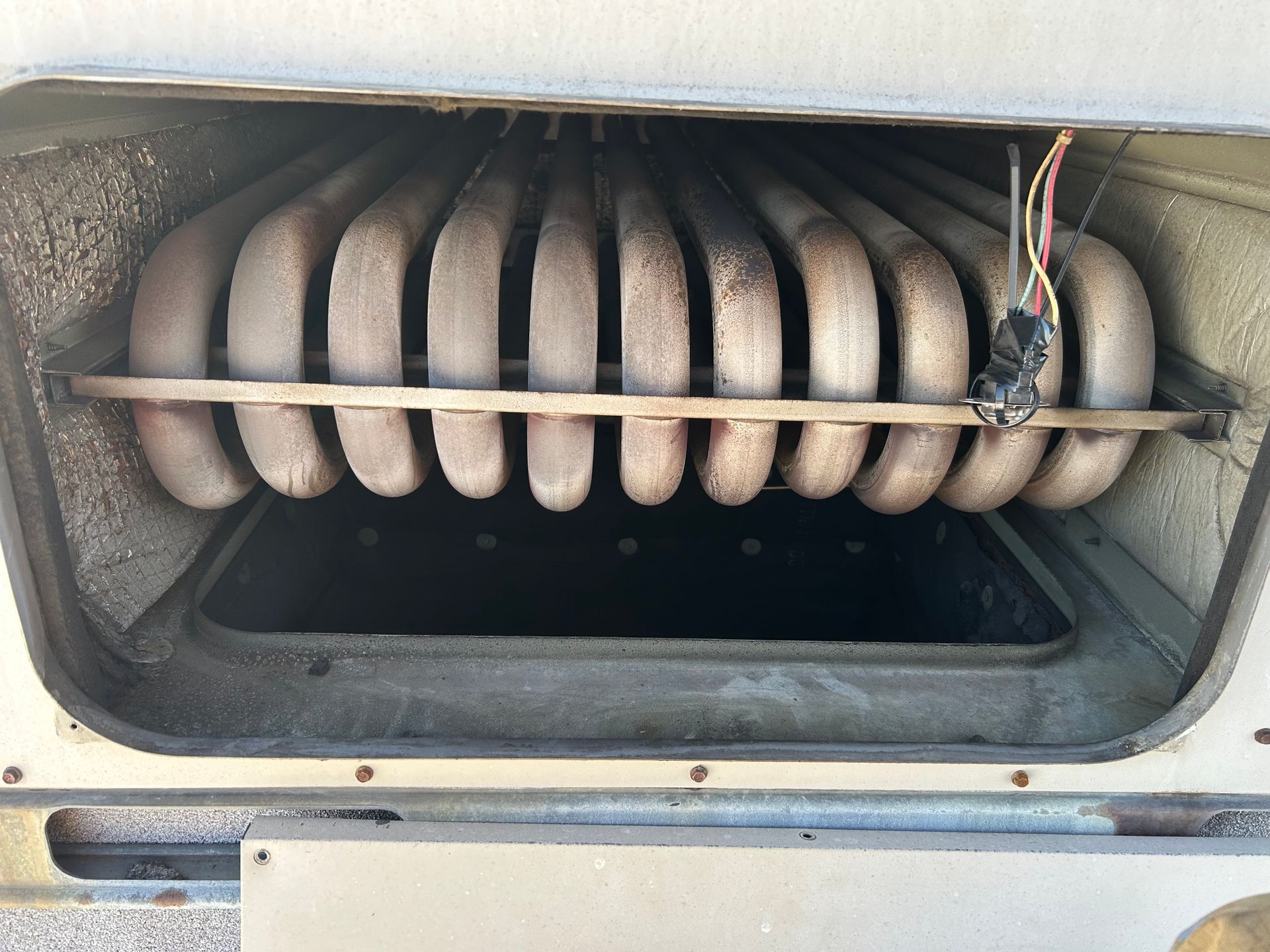A row of metal furnace heat exchanger tubes inside an open heating unit.