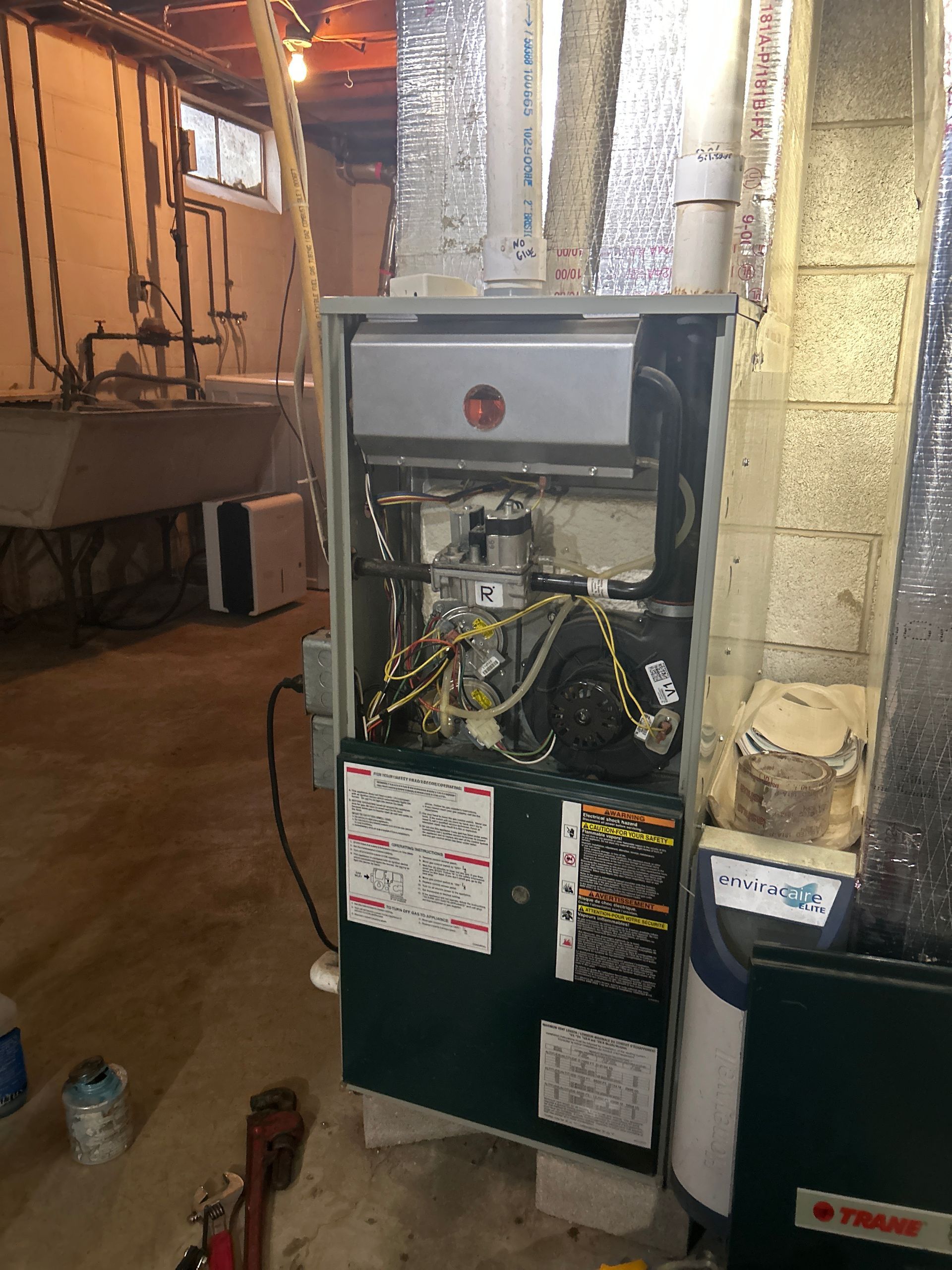 A partially disassembled furnace with internal components and wiring exposed, located in a basement utility area.