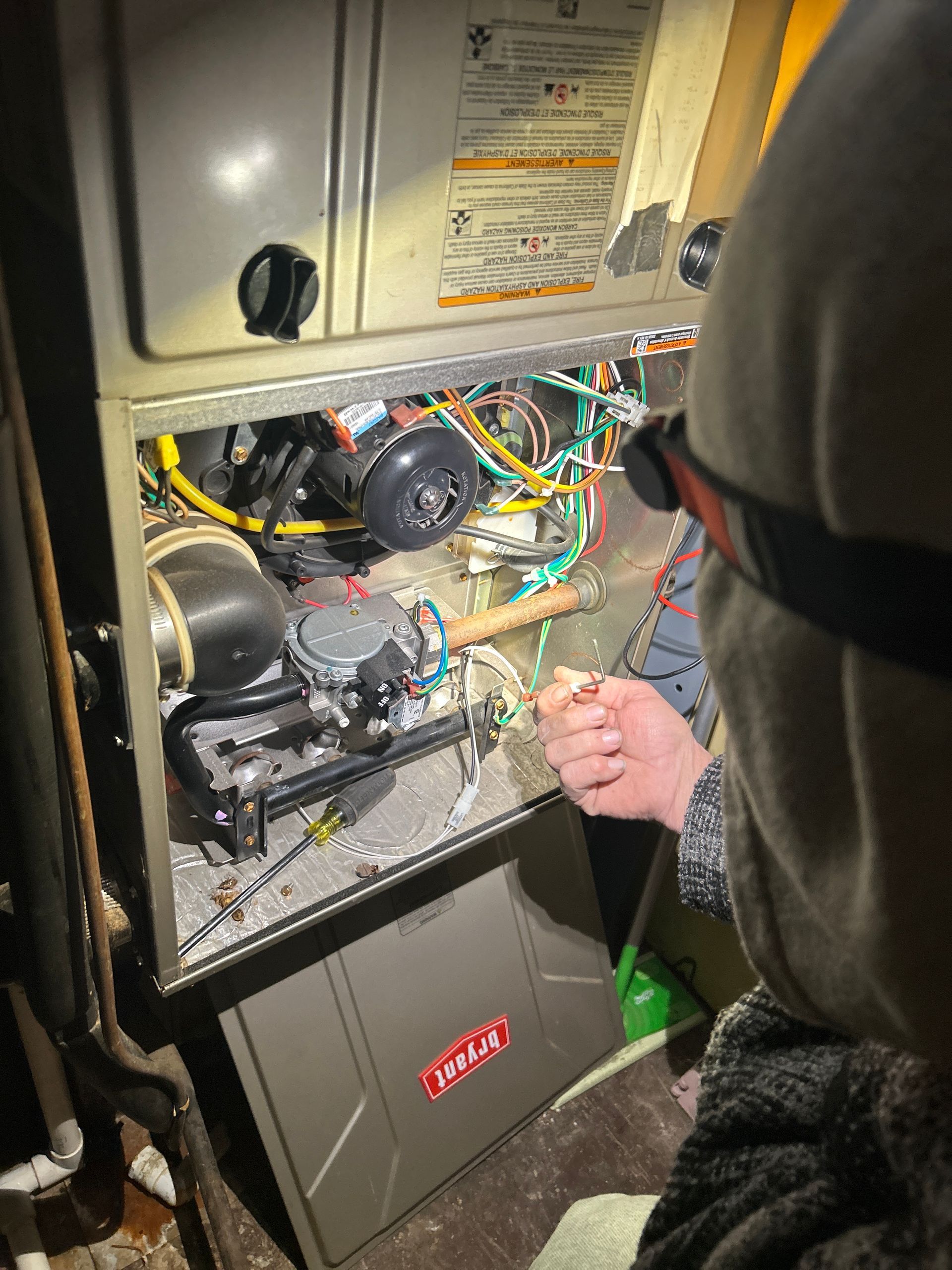 A technician inspects a Bryant furnace, examining the interior wiring and gas valve assembly.