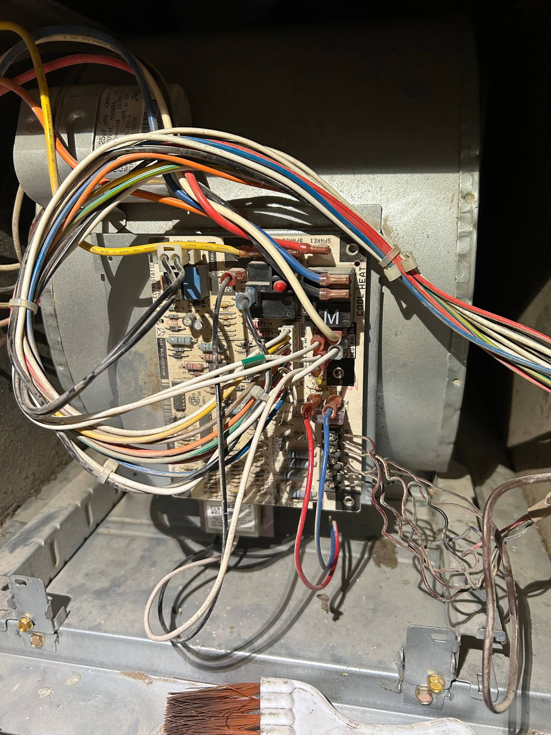 A circuit board and wiring assembly mounted on the side of a metal furnace blower unit inside a dark enclosure.
