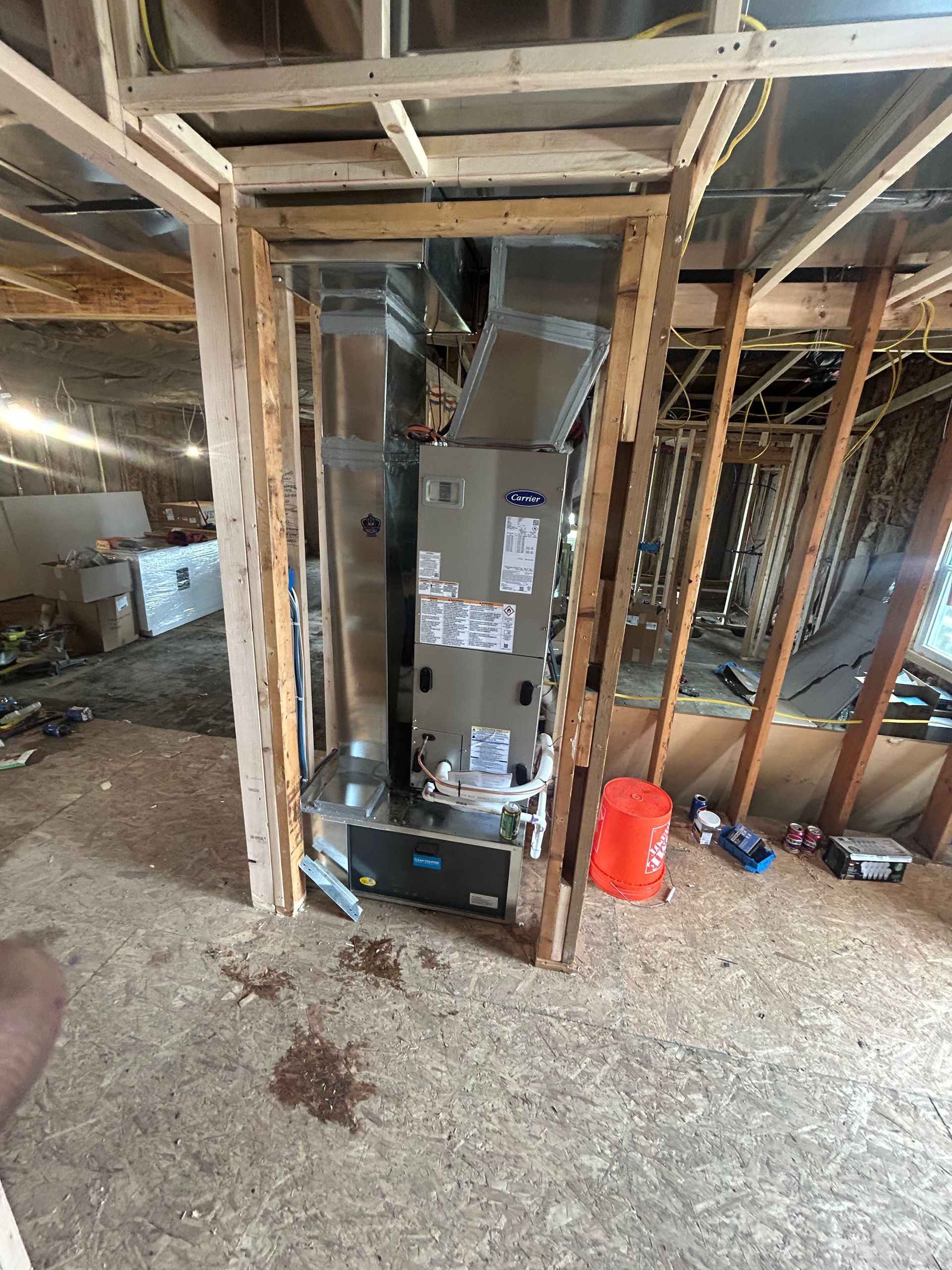 A furnace and ductwork installation inside an unfinished wood-framed wall in a building under construction.