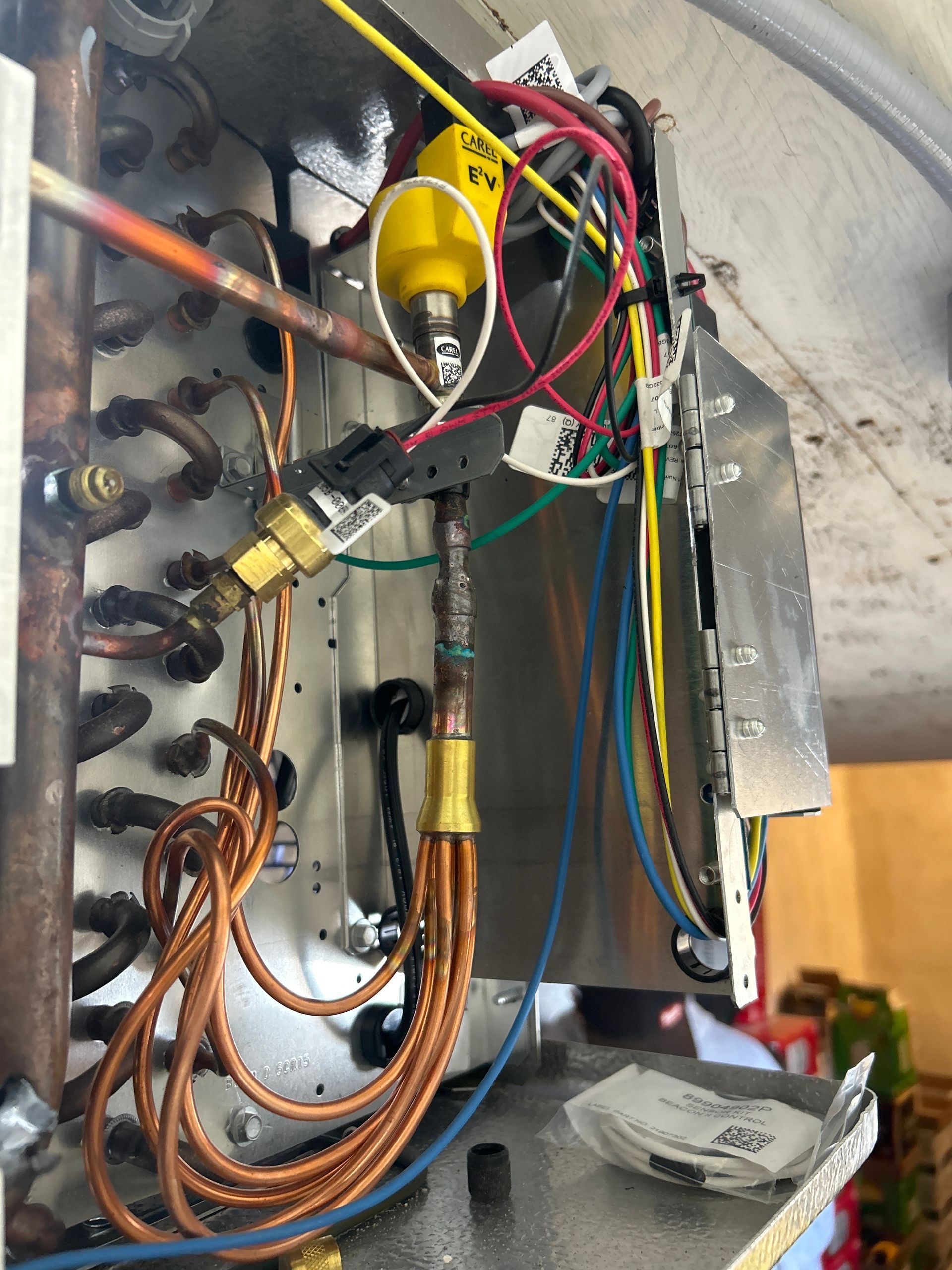 A close-up view of the interior components of an HVAC unit, showing copper tubing, electrical wiring, and sensors.