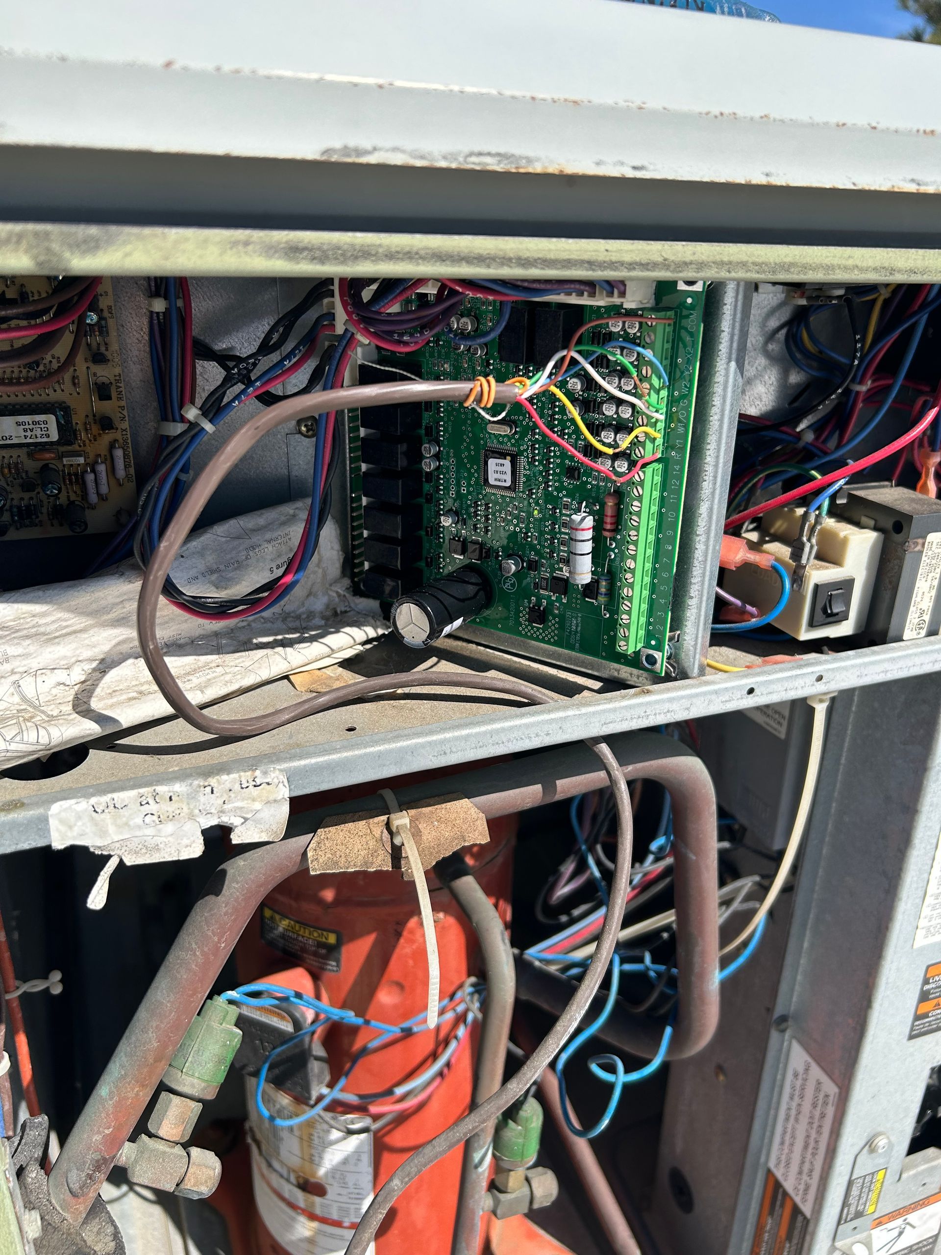 Open panel of an industrial HVAC unit revealing electrical circuit boards, wiring, and a large orange compressor tank.