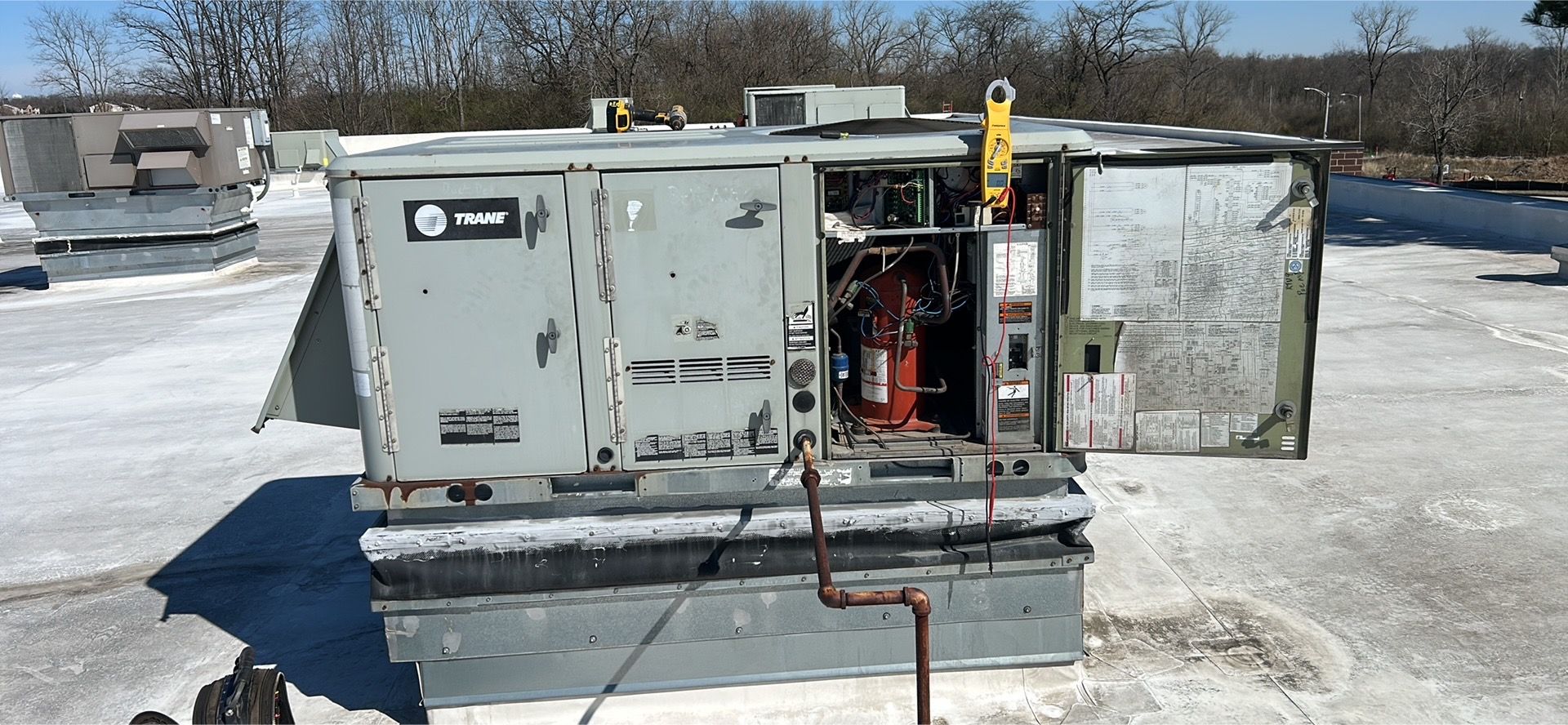A grey commercial rooftop HVAC unit with its side service panel open, revealing internal components and a pipe.
