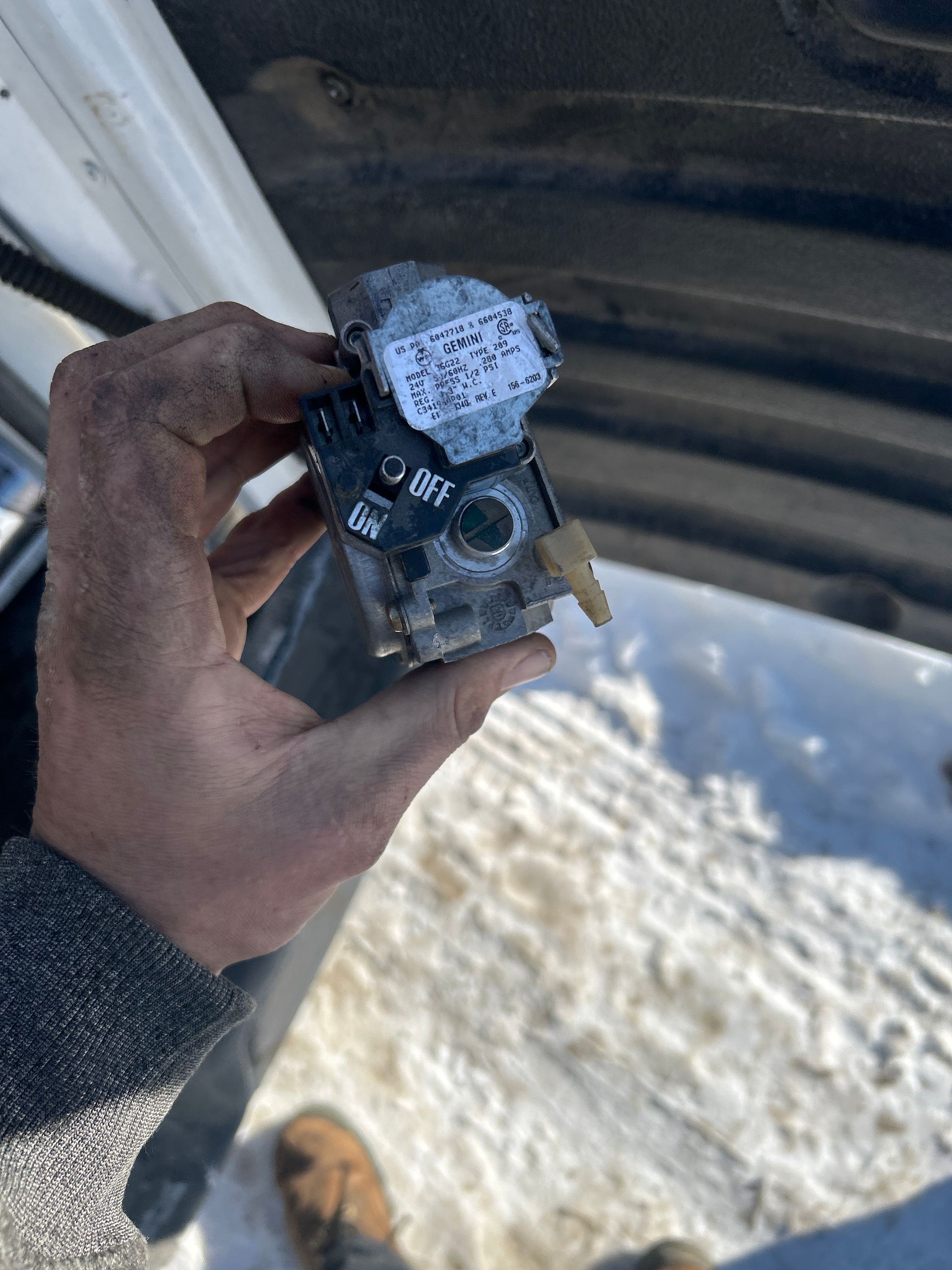 A hand holds a dirty metallic mechanical part with a dial labeled 