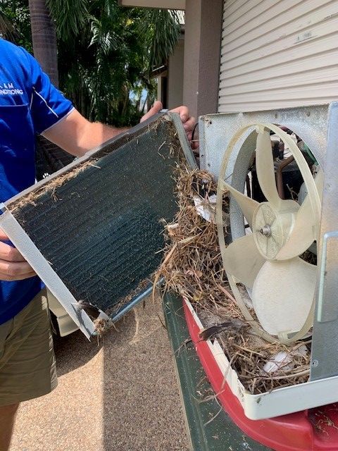 A Man is Holding a Dirty Air Conditioner and a Fan — Legit Air Conditioning in Garbutt, QLD