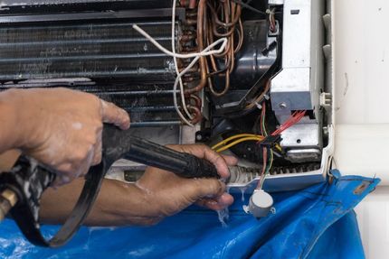 A Person is Cleaning an Air Conditioner With a Spray Bottle — Legit Air Conditioning in Garbutt, QLD