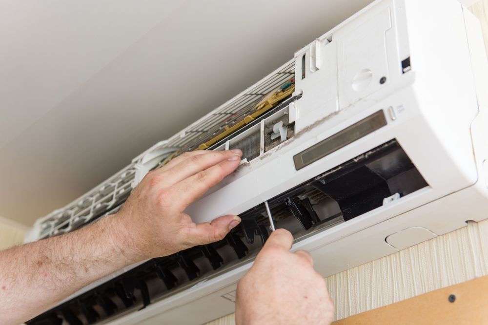 A Man is Fixing an Air Conditioner With a Screwdriver — Legit Air Conditioning in Garbutt, QLD
