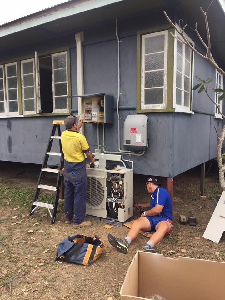 Two Men Are Working on an Air Conditioner Outside of a Blue House — Legit Air Conditioning in Garbutt, QLD