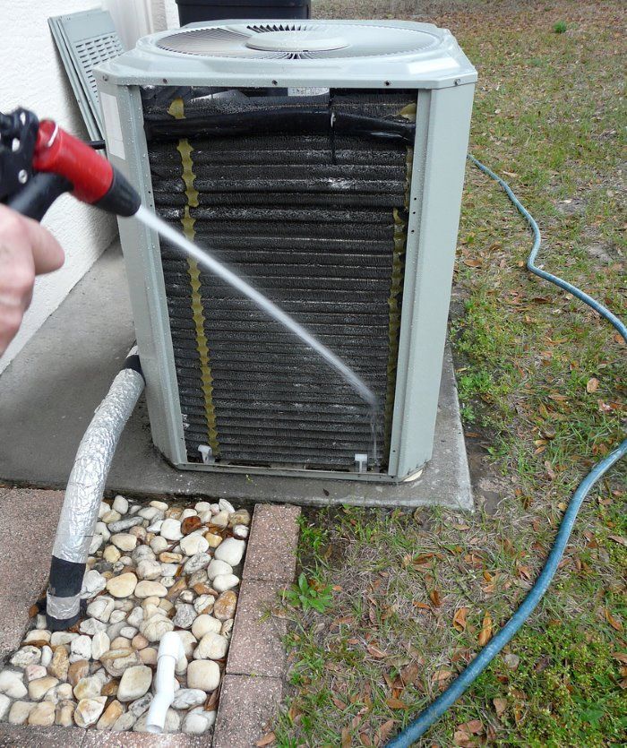 A Person is Cleaning an Air Conditioner With a Hose — Legit Air Conditioning in Garbutt, QLD