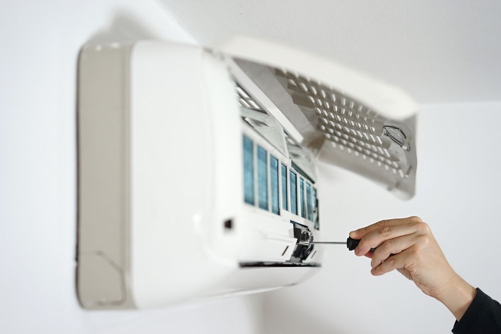 A Person is Fixing an Air Conditioner With a Screwdriver — Legit Air Conditioning in Garbutt, QLD