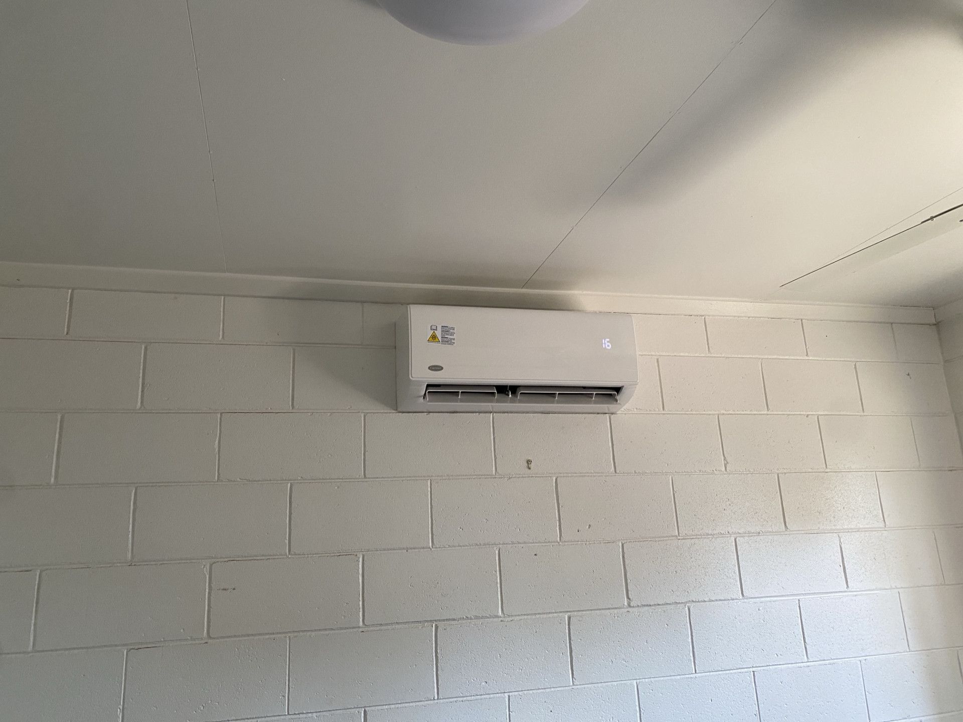 A White Air Conditioner is Mounted on a White Brick Wall — Legit Air Conditioning in Garbutt, QLD