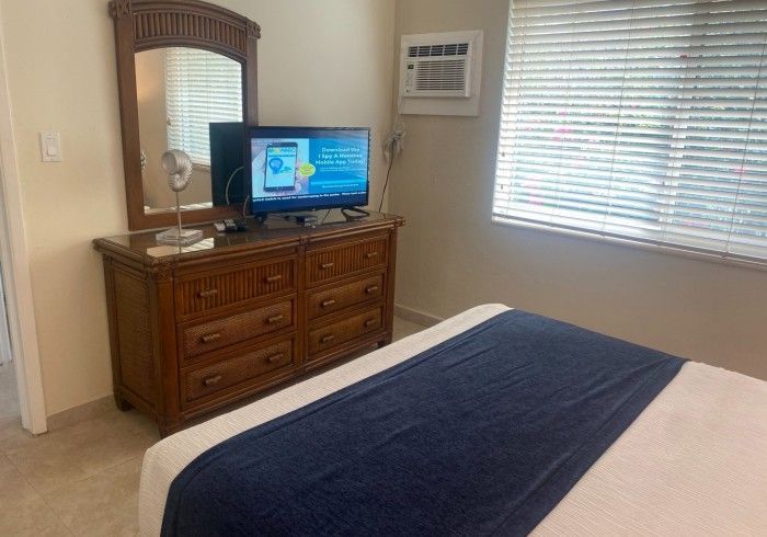 Bedroom with dresser, TV, window blinds, and bed with a dark blue runner.