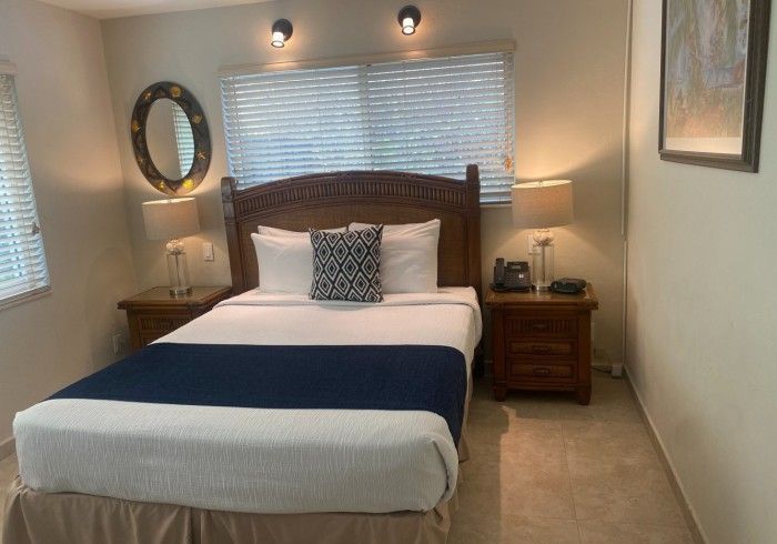 Cozy bedroom with a bed, dark blue runner, wooden nightstands, lamps, and a window with blinds.