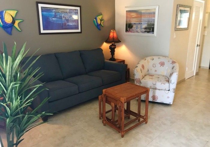 Cozy living room with navy sofa, floral armchair, wooden tables, lamp, and framed wall art.