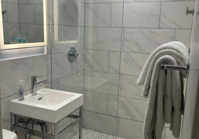 Modern tiled bathroom with glass shower, white sink, and folded towels on a rack