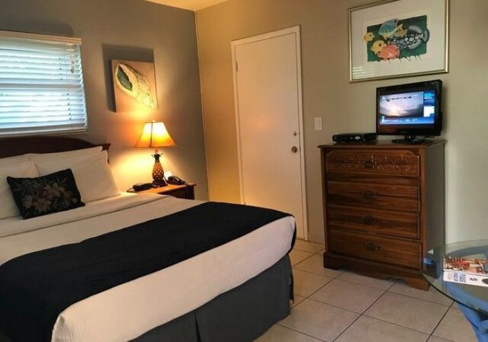 Small bedroom with a made bed, nightstand lamp, dresser, wall art, and TV.