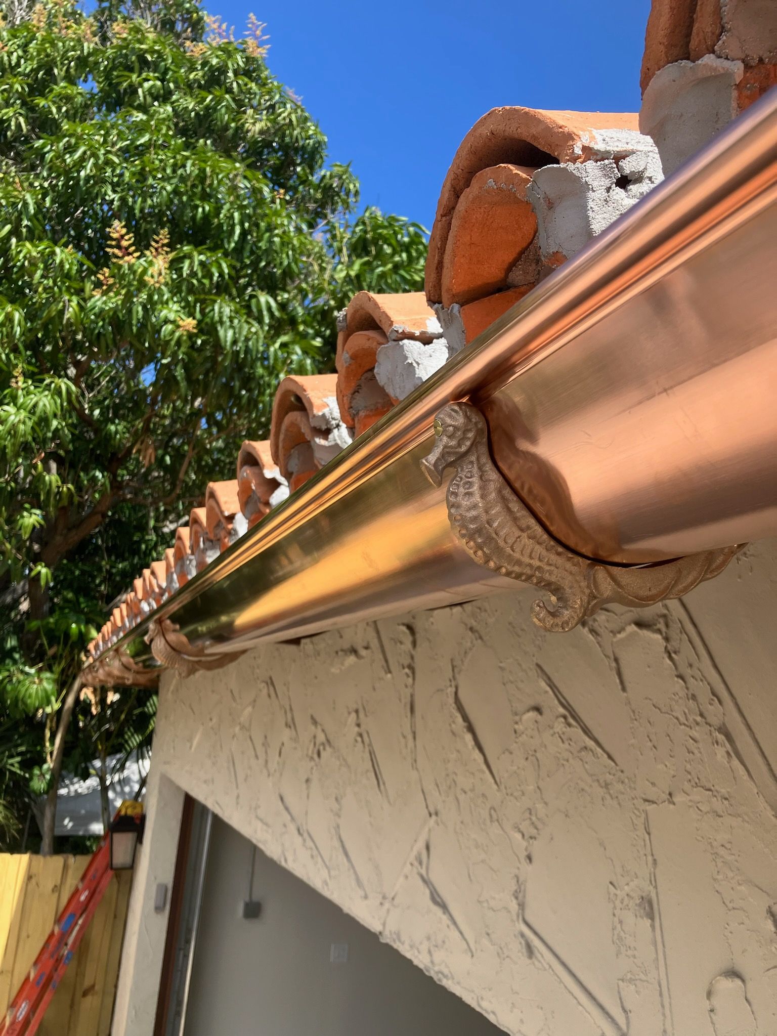 Brown gutters on a wooden house with a visible downspout, against a backdrop of autumn leaves.