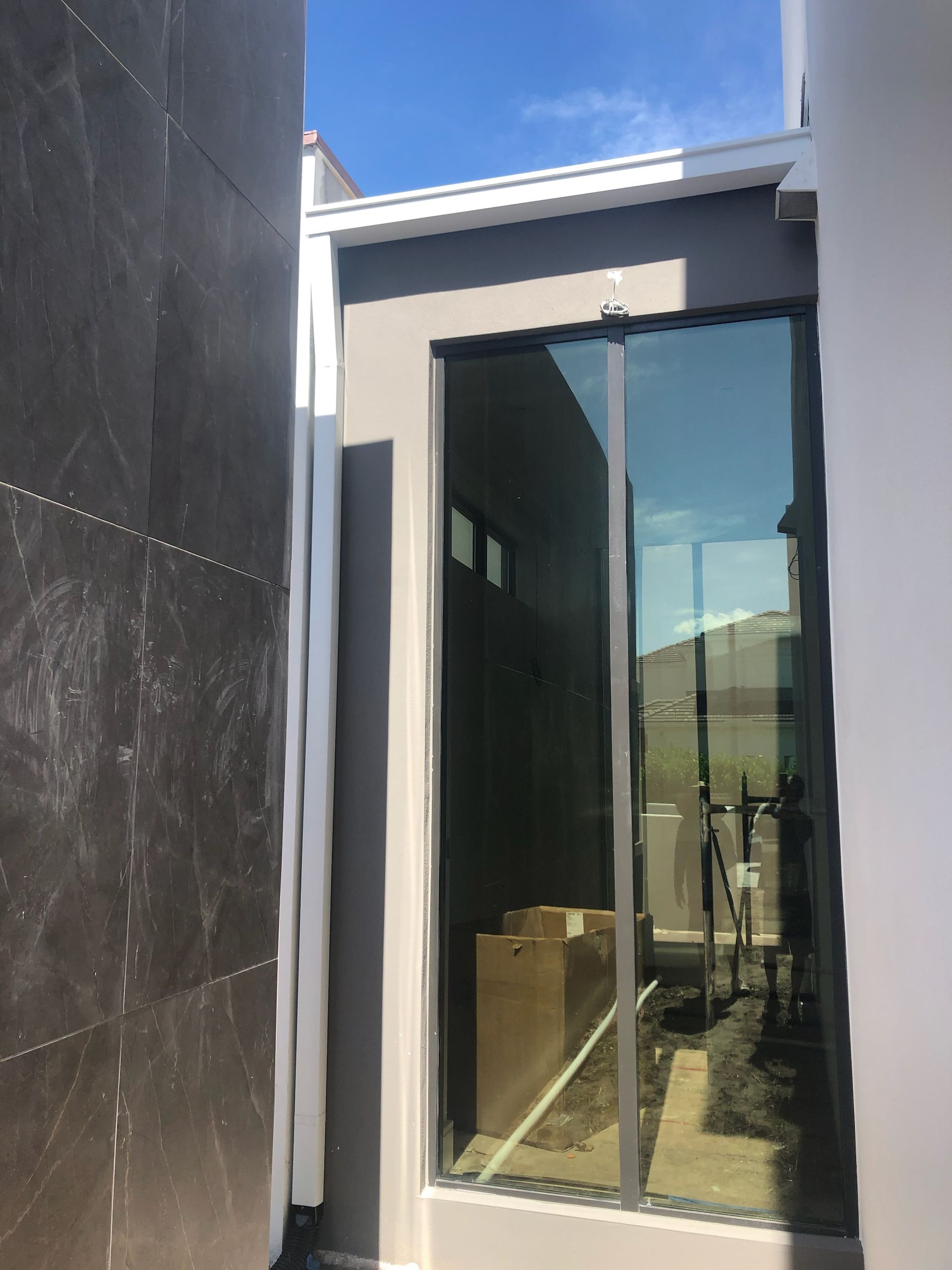 Beige rain gutter on a yellow stucco house corner against a blue sky.