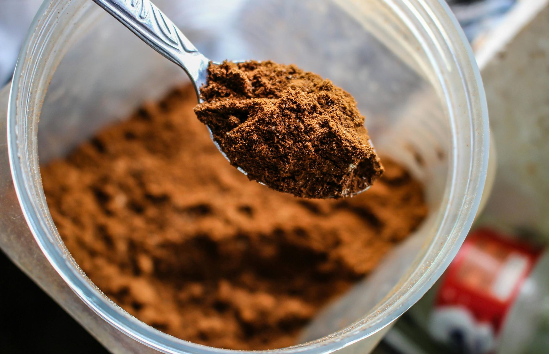 A spoon is taking a scoop of cocoa powder out of a plastic container.