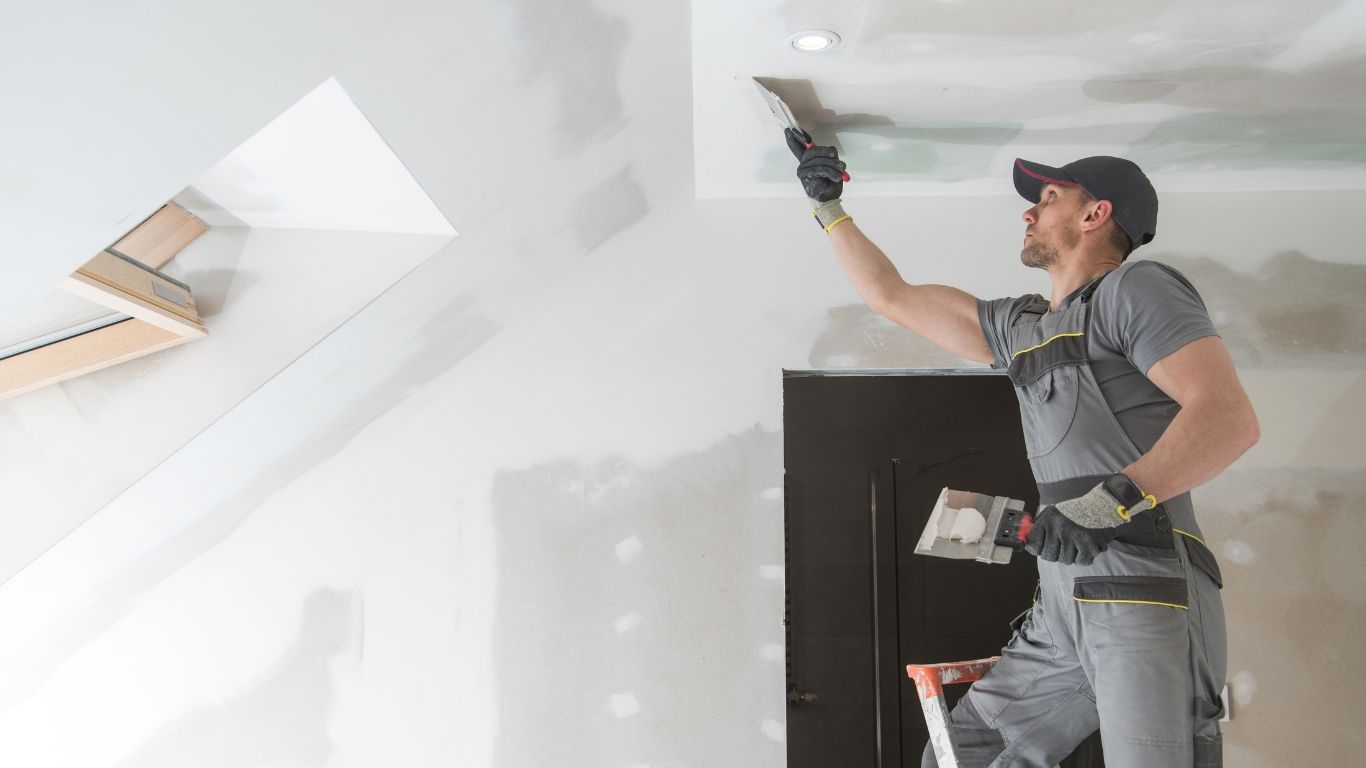 A man is plastering a ceiling with a spatula.