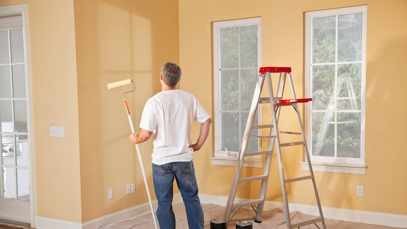 A man is standing in a room holding a paint roller.