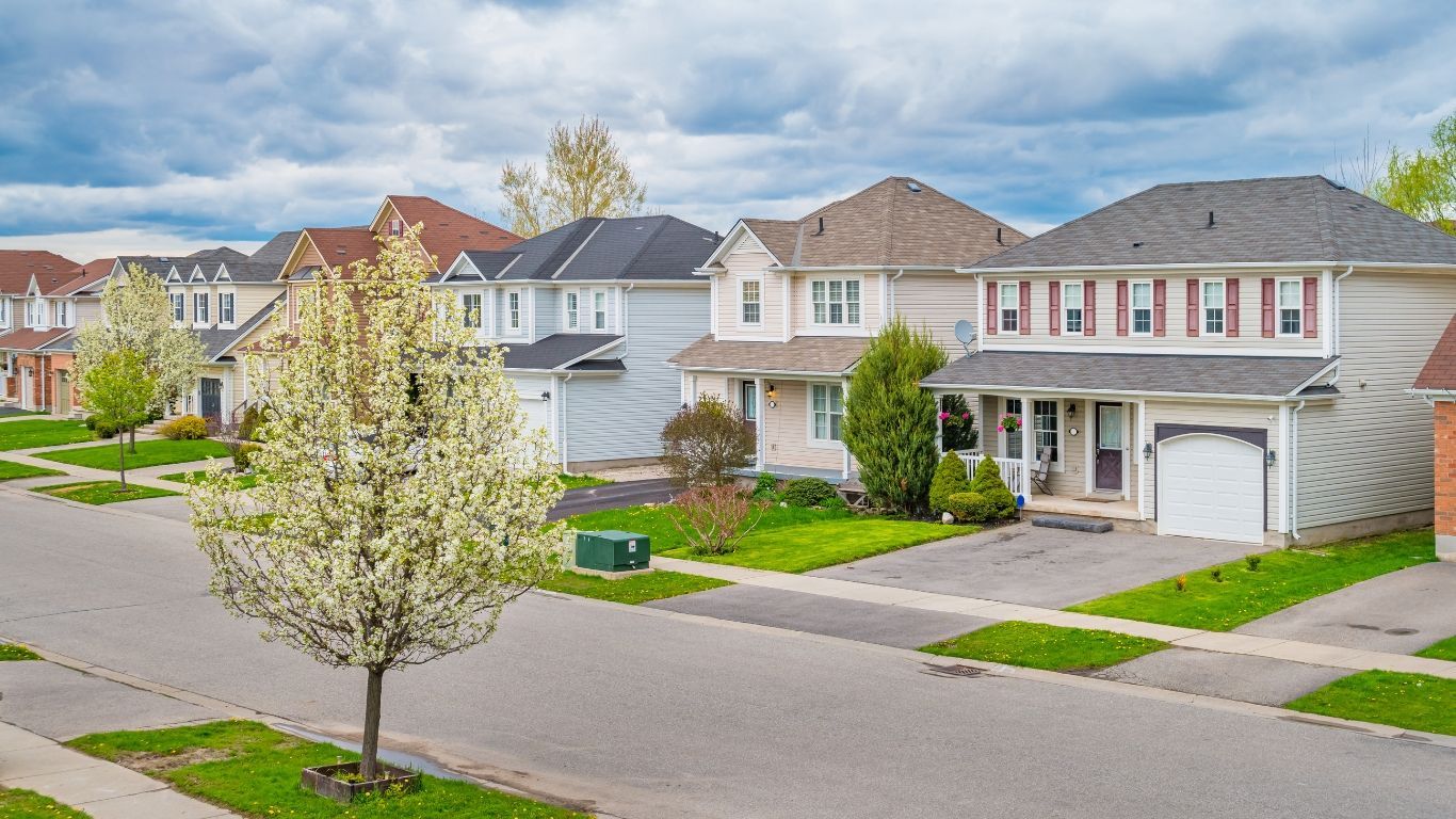 A row of houses in a residential neighborhood with a tree in the middle of the street.