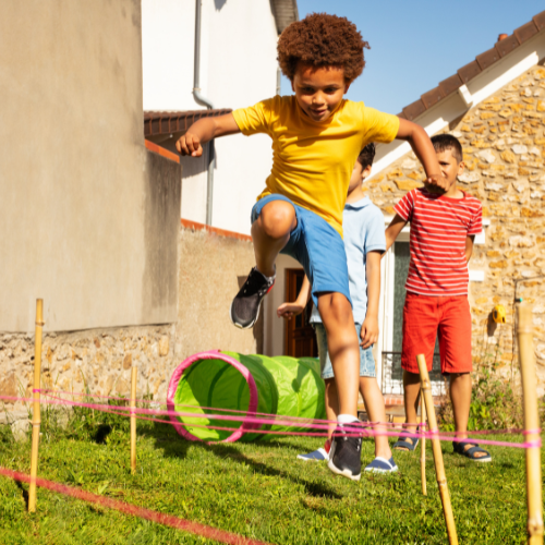 A boy in a yellow shirt is jumping over a rope