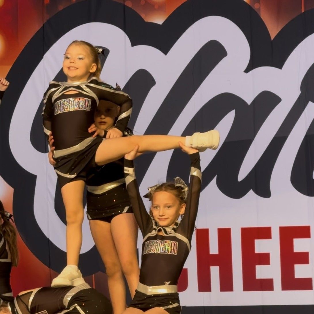 Cheerleaders perform in front of a sign that says cheer