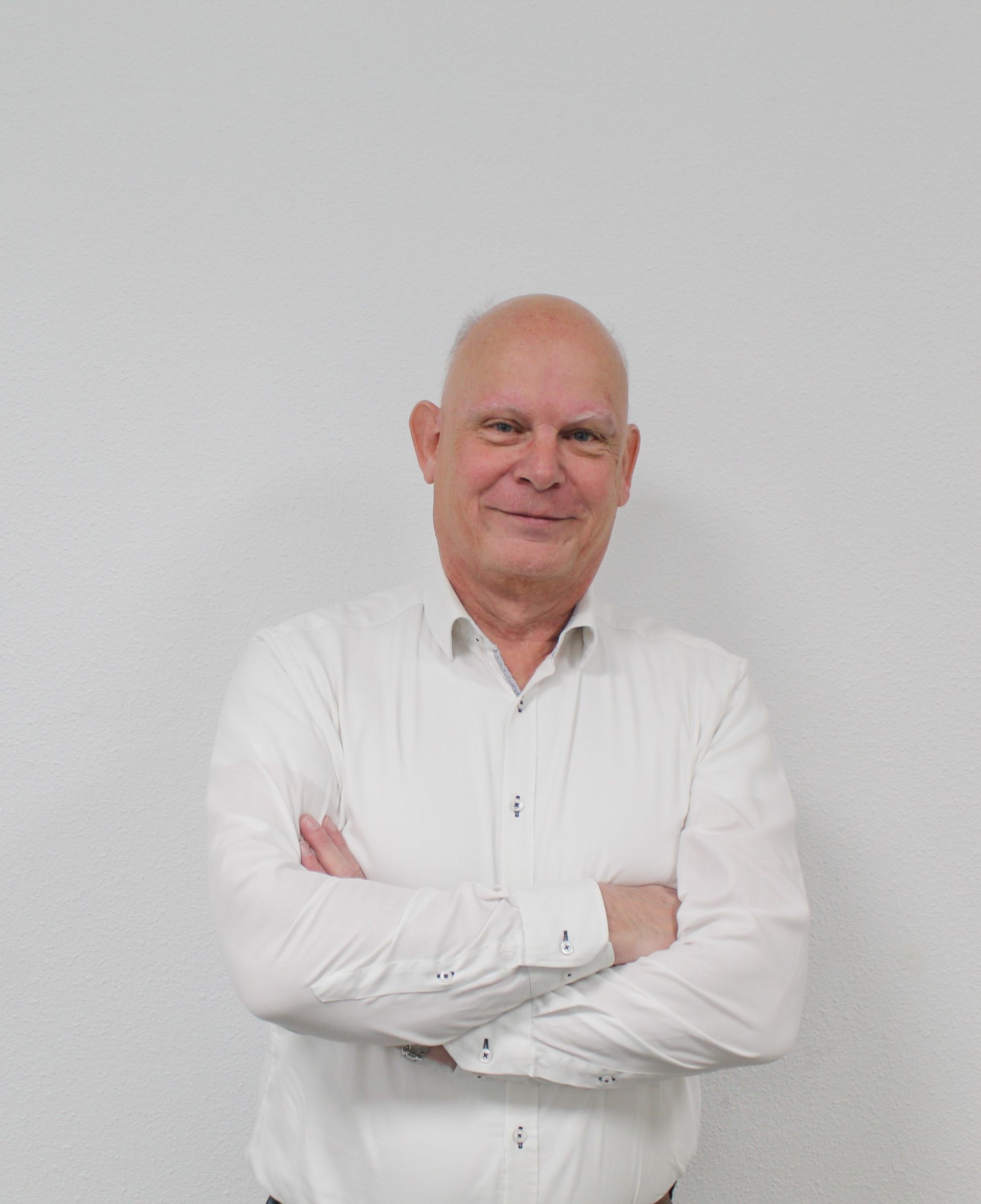 Een kale man in een wit overhemd staat met zijn armen over elkaar.