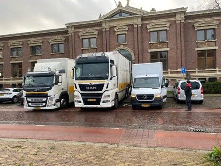 Een groep vrachtwagens staat geparkeerd voor een groot gebouw.