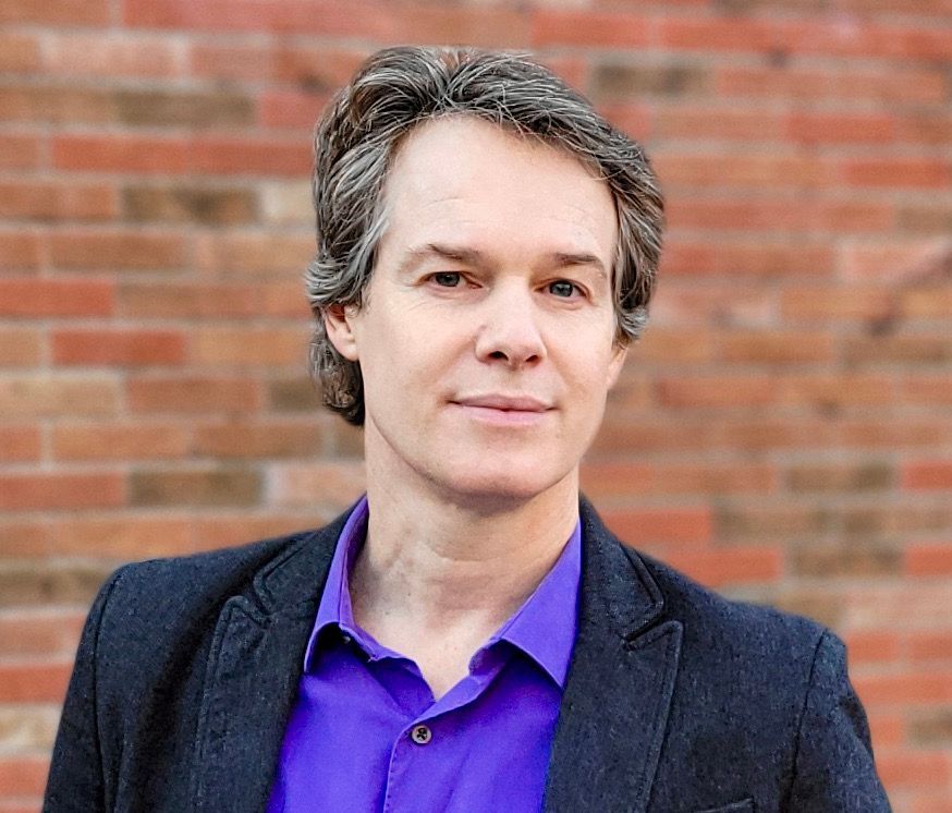 Image of Paul Van Dyck standing in front of brick wall