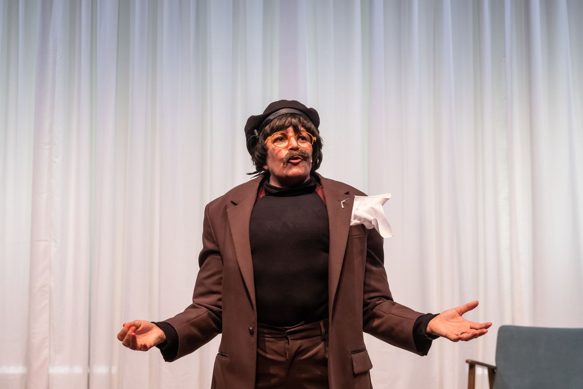 A person on stage gestures confused. White curtains behind them