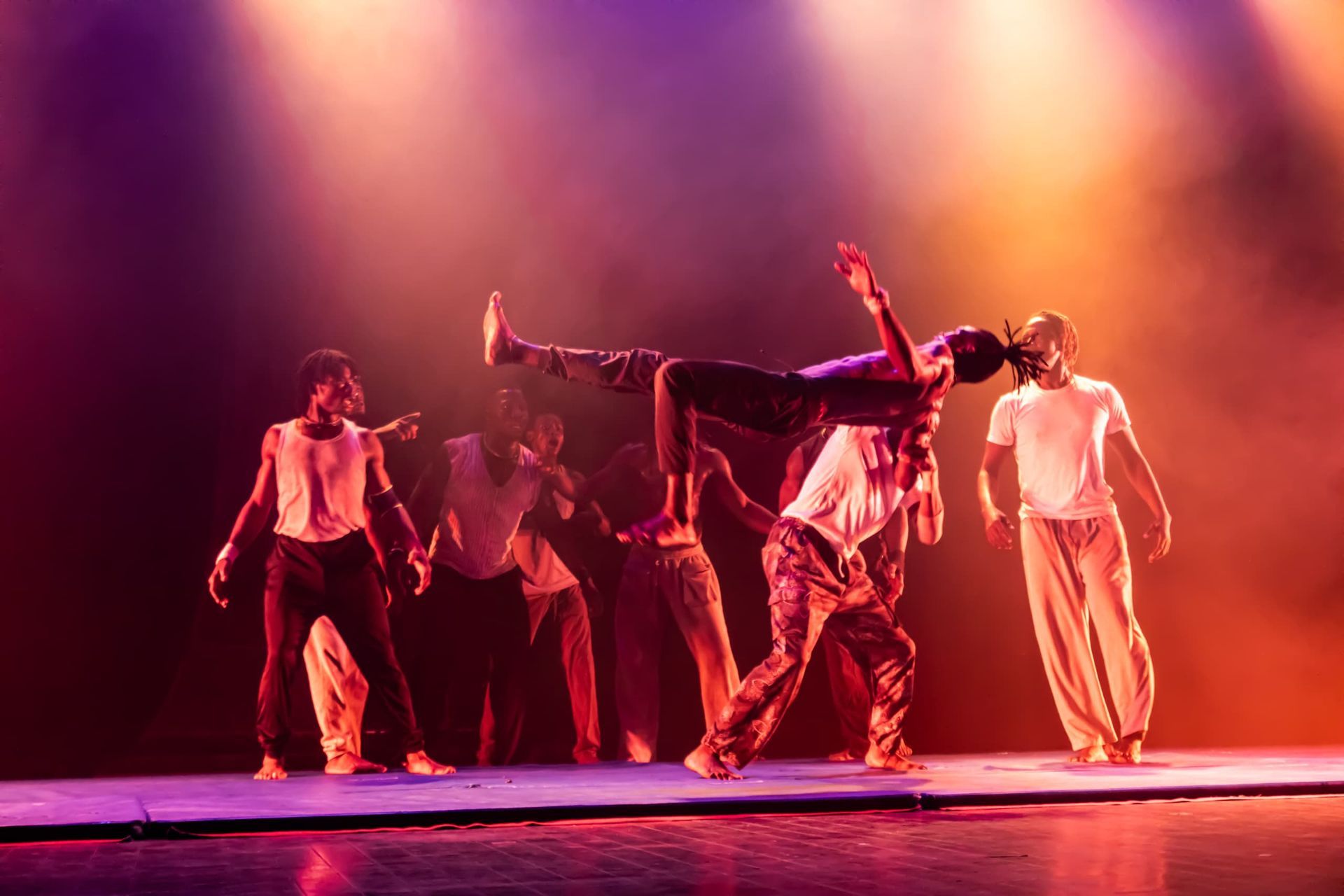 One person flipping on a stage. Many dancers are behind them. Dramatic red and yellow lighting.