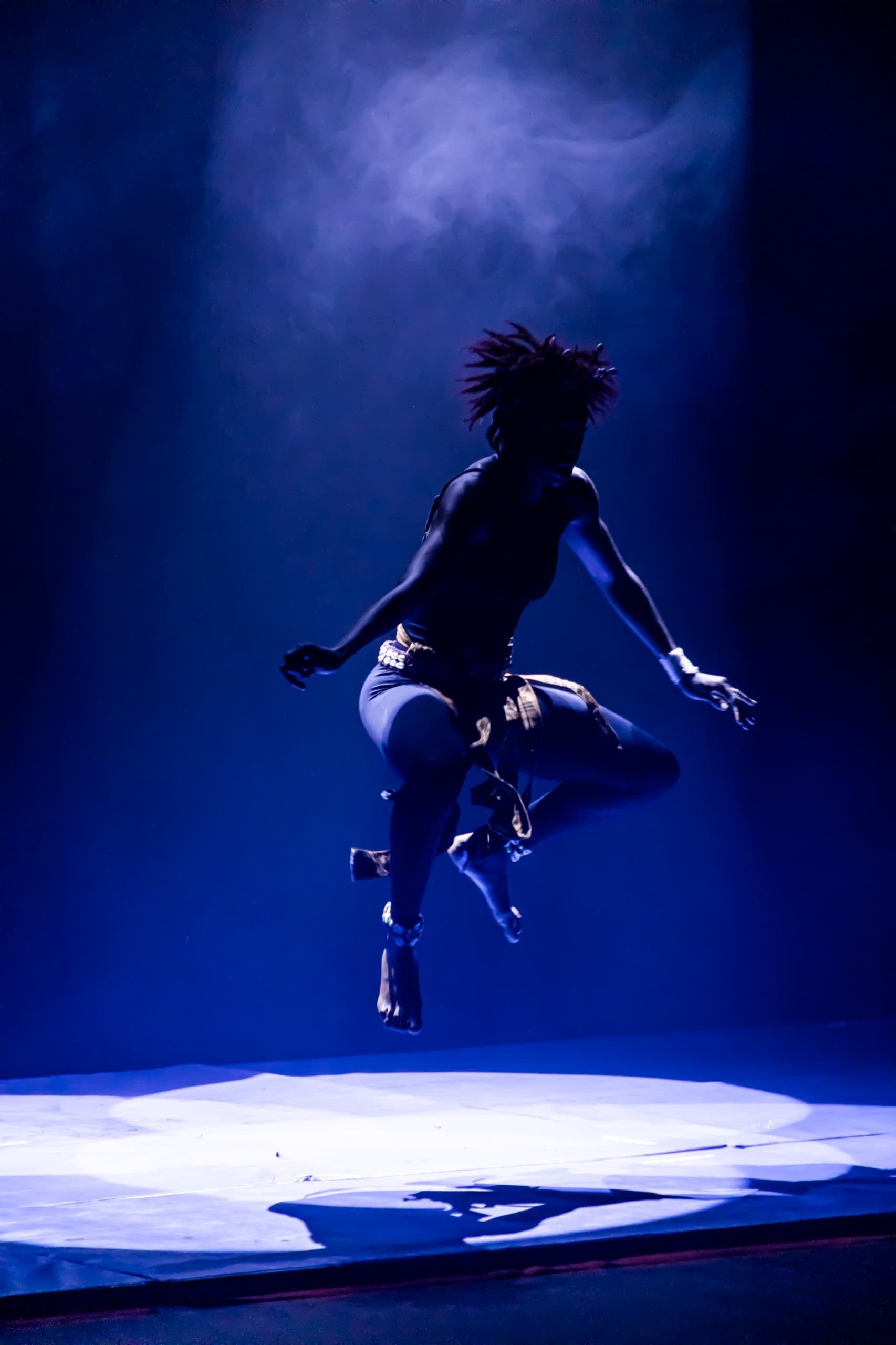 One person jumping on stage in dramatic blue lighting. Darkness around them.