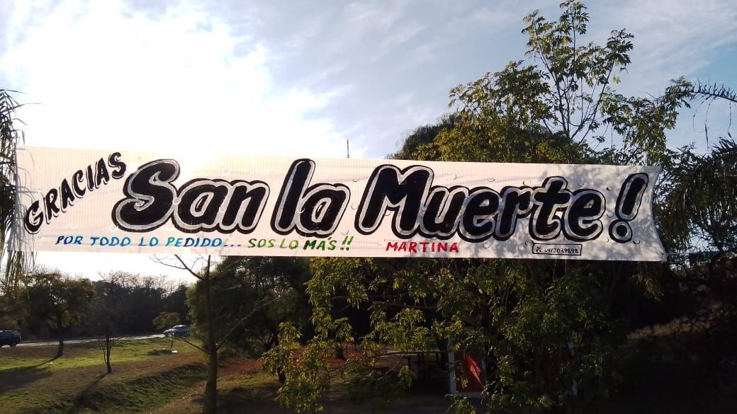 Una pancarta que dice gracias san la muerte está colgada de un árbol.