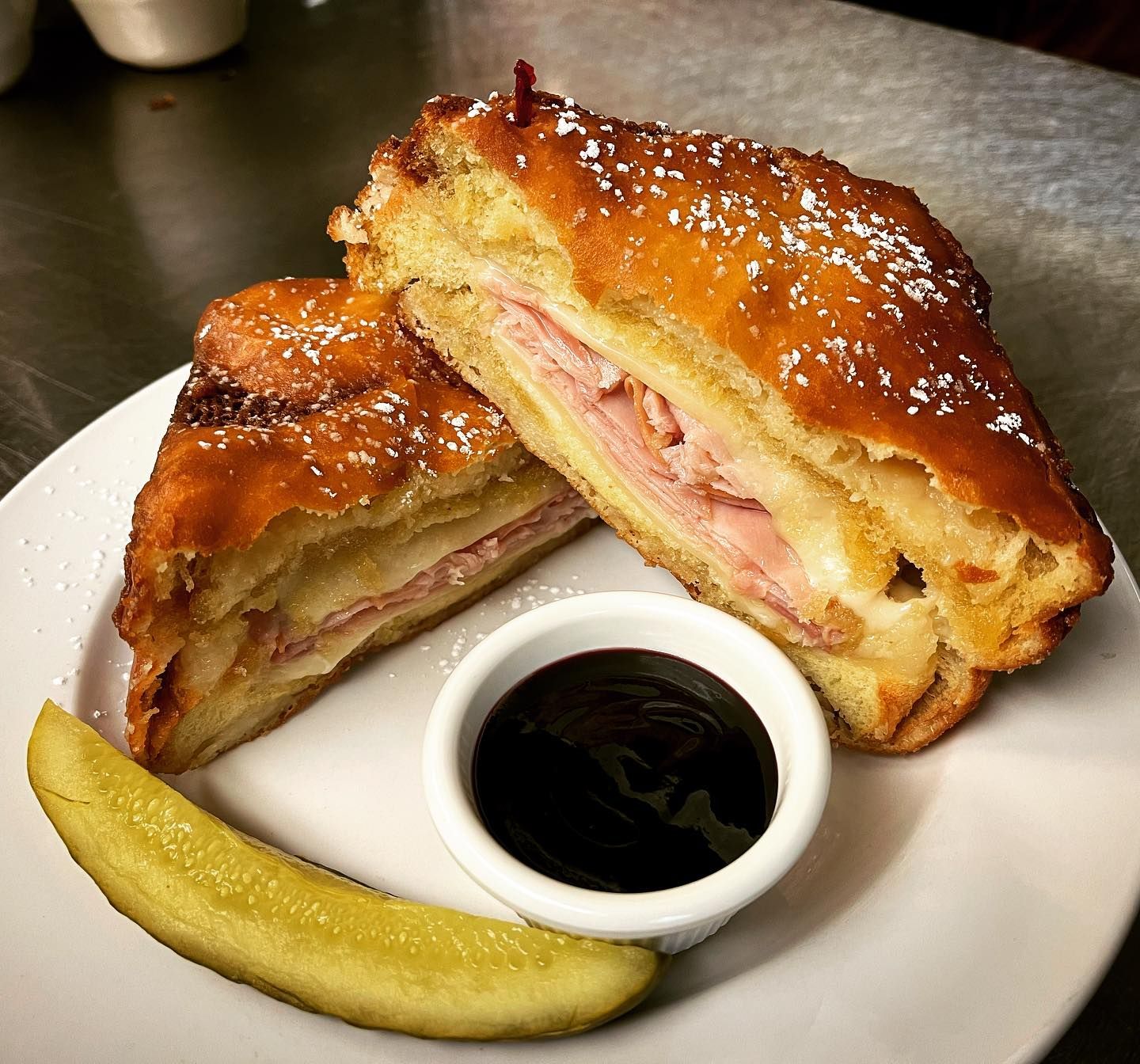 A sandwich on a plate with a pickle and dipping sauce