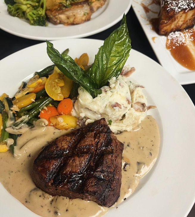 A white plate topped with a steak and mashed potatoes